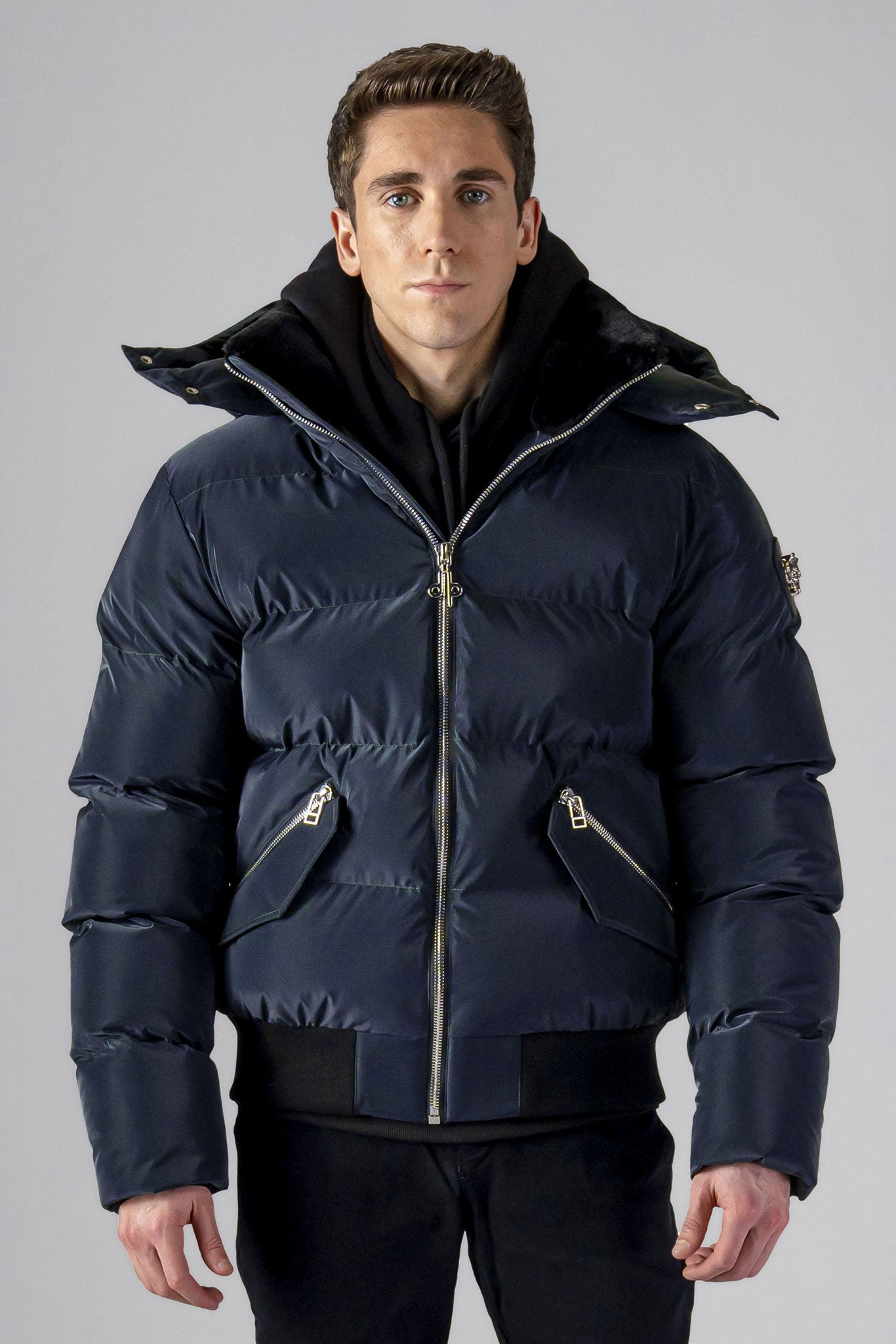 Woodpecker Men's Woody Bomber Winter coat. High-end Canadian designer winter coat for men in "Blue Diamond" colour. Woodpecker cruelty-free winter coat designed in Canada. Men's heavy weight short length premium designer jacket for winter. Superior quality warm winter coat for men. Moose Knuckles, Canada Goose, Mackage, Montcler, Will Poho, Willbird, Nic Bayley. Shiny parka. Stylish winter jacket. Designer winter coat.