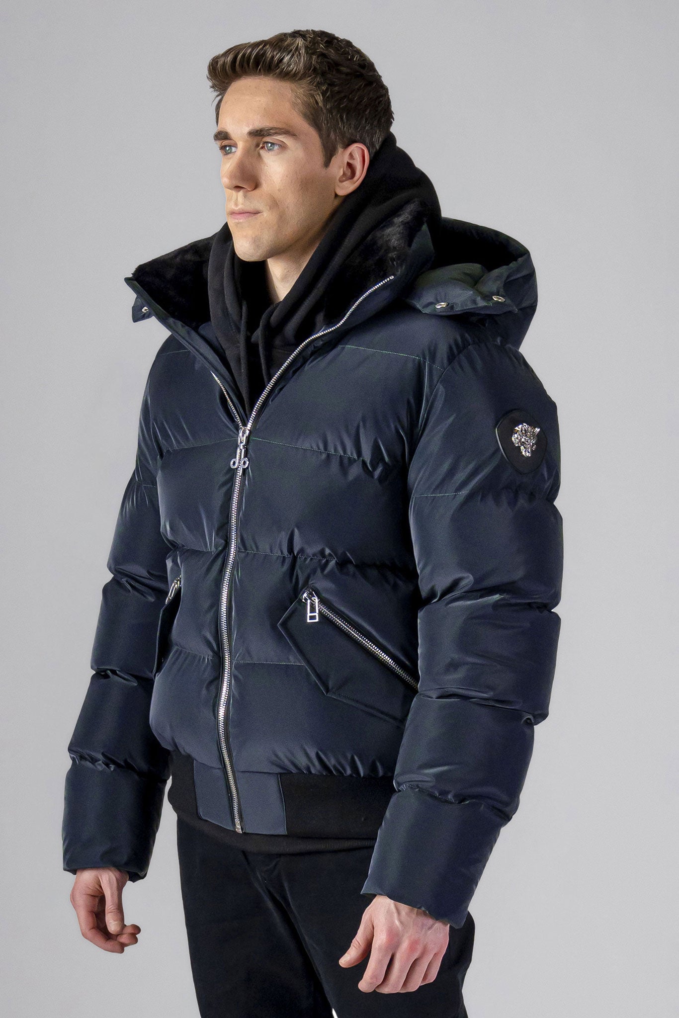 Woodpecker Men's Woody Bomber Winter coat. High-end Canadian designer winter coat for men in "Blue Diamond" colour. Woodpecker cruelty-free winter coat designed in Canada. Men's heavy weight short length premium designer jacket for winter. Superior quality warm winter coat for men. Moose Knuckles, Canada Goose, Mackage, Montcler, Will Poho, Willbird, Nic Bayley. Shiny parka. Stylish winter jacket. Designer winter coat.